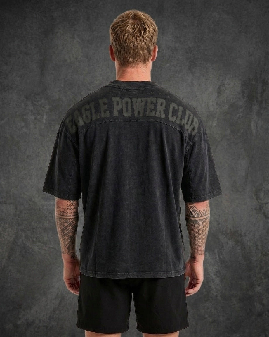 Person wearing a black t-shirt with 'Eagle Power Club' text on the back against a dark background